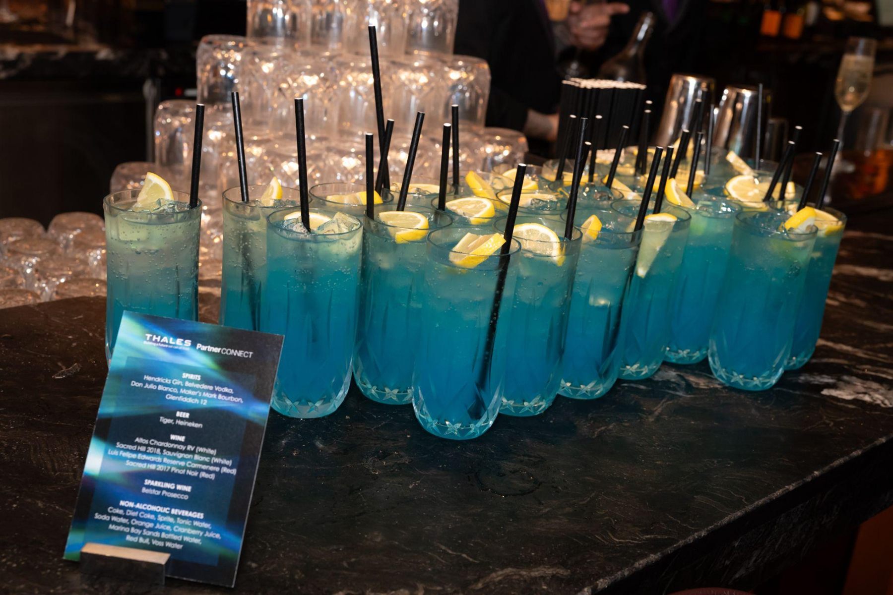 Signature cocktails on a bar counter beside a Thales PartnerCONNECT menu card