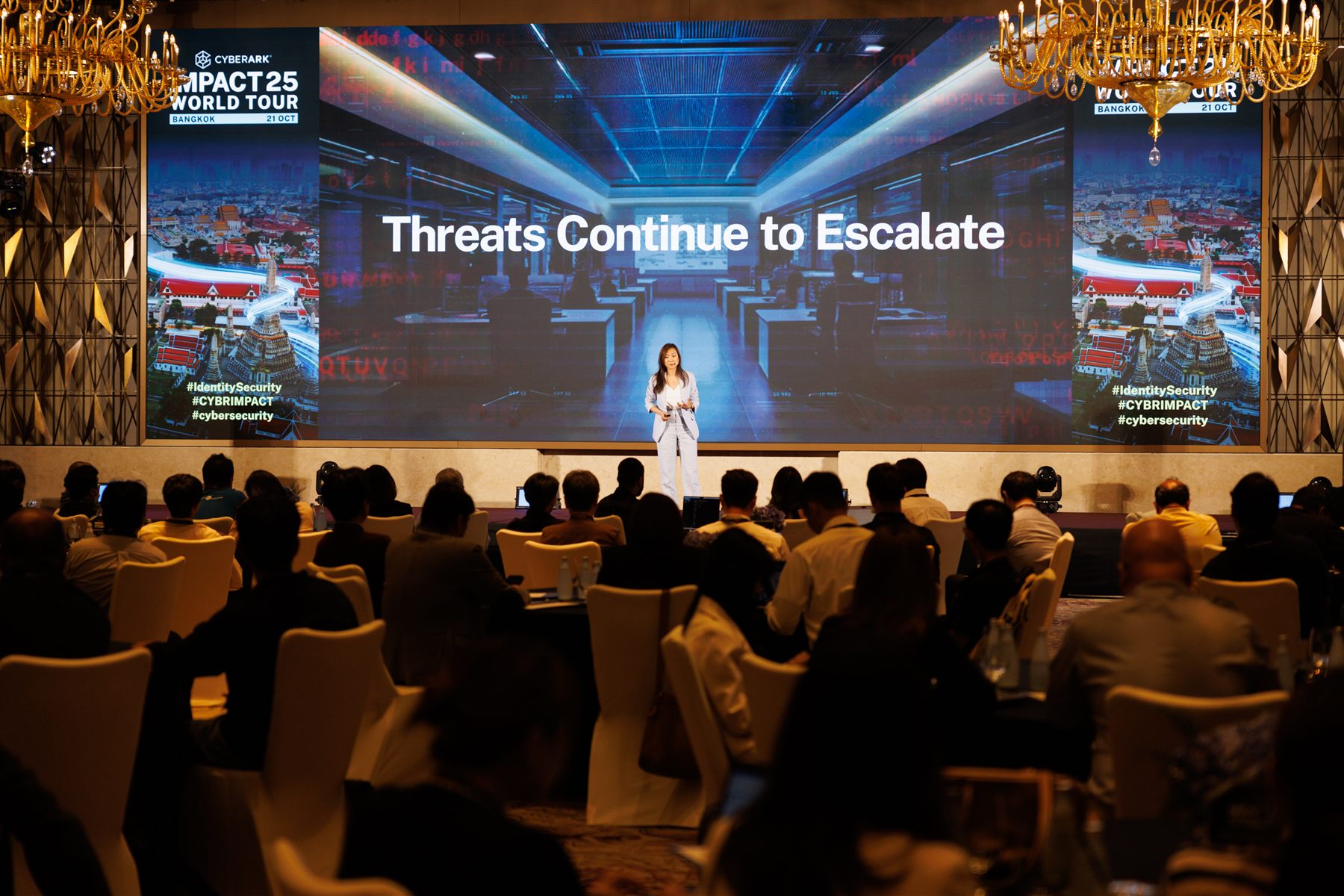 The Bangkok main stage under ballroom chandeliers, a speaker mid-session against a full-width screen