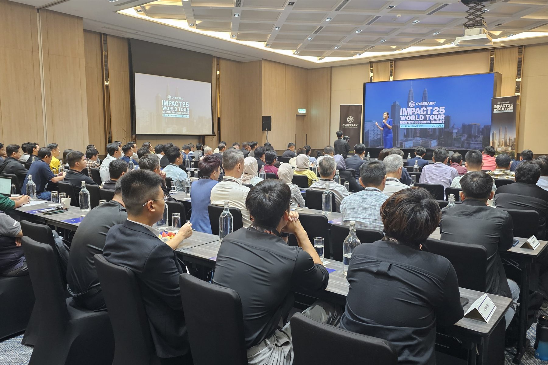 A full plenary room in Kuala Lumpur, twin stage screens carrying the event identity