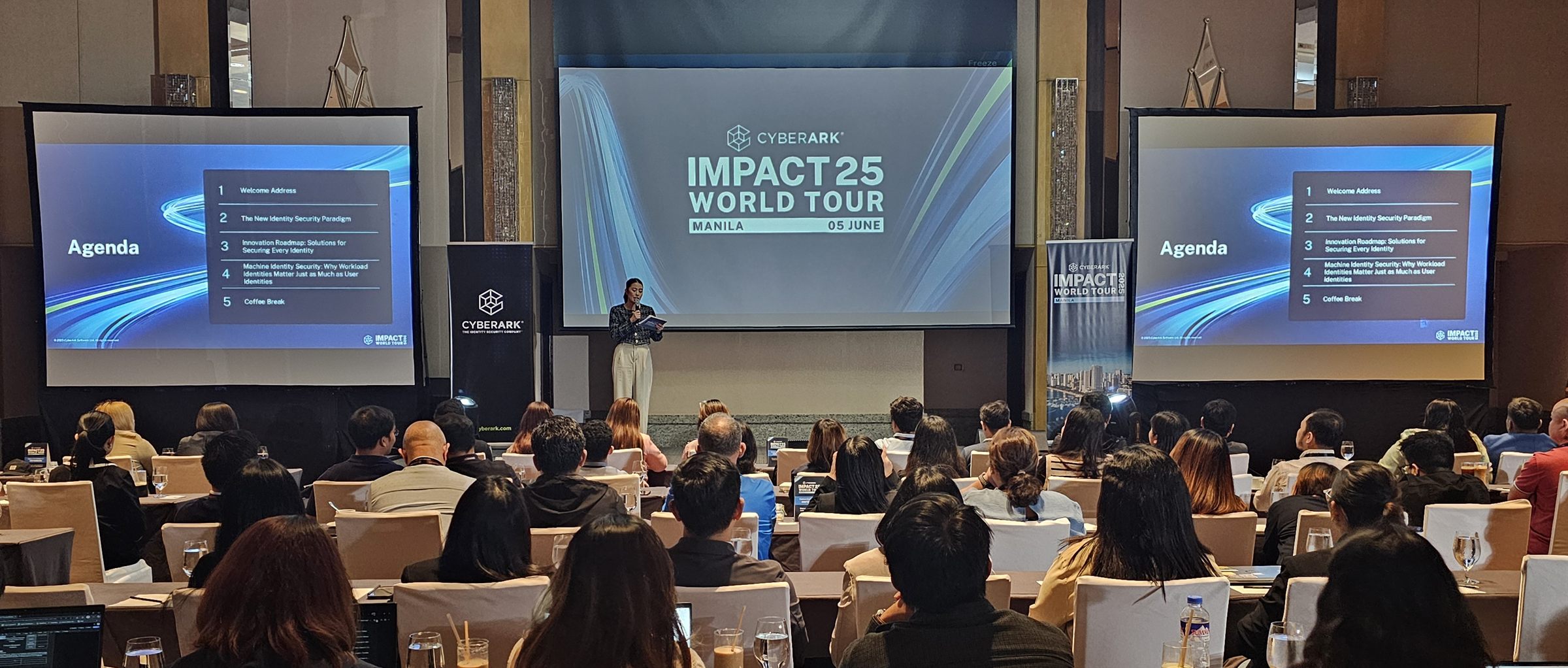Welcome address on the triple-screen Manila stage, the agenda mirrored either side of the IMPACT25 title card