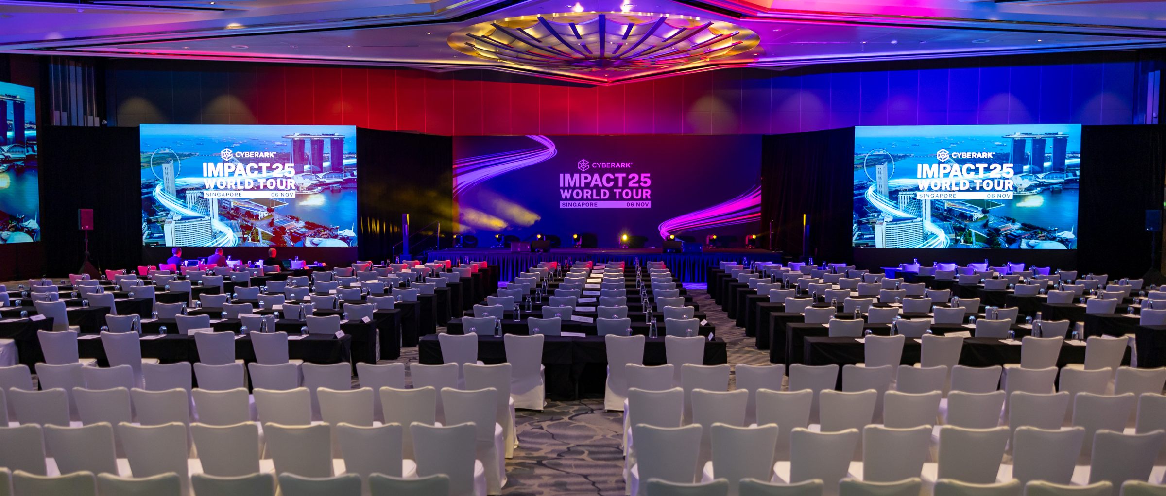 The IMPACT25 World Tour ballroom in Singapore before doors open, triple screens carrying the Singapore edition branding above rows of dressed seating