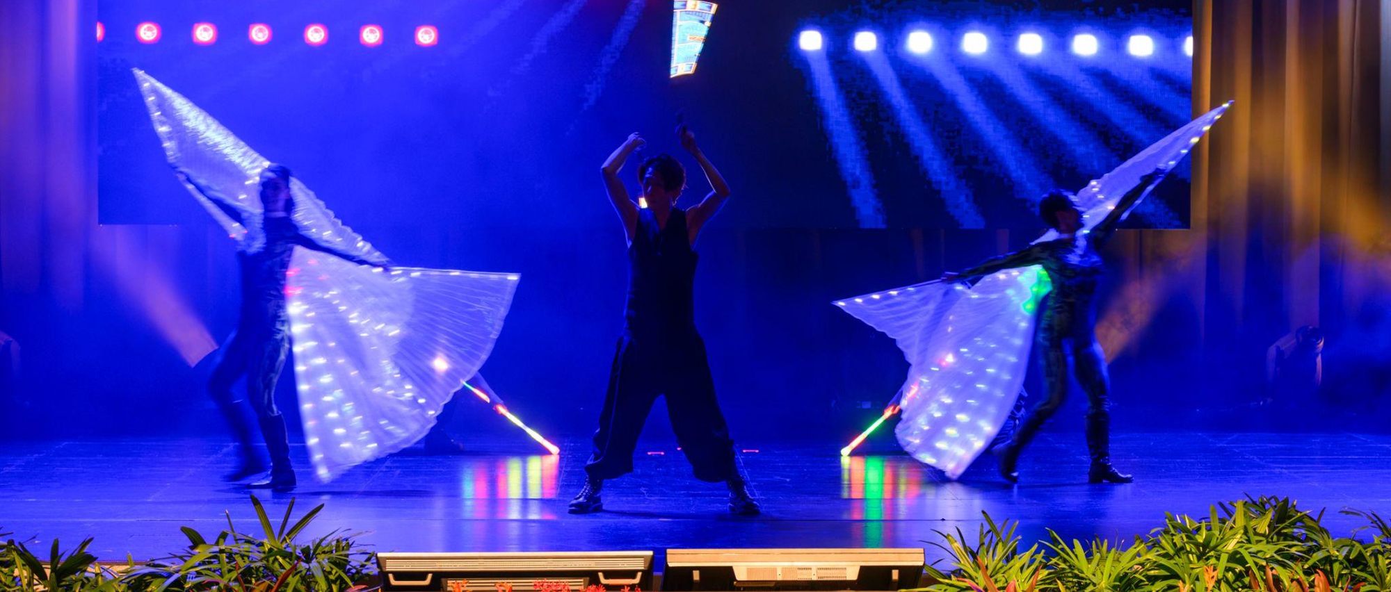 The opening performance: dancers in illuminated wing costumes lit blue across the stage, planting dressing the stage edge