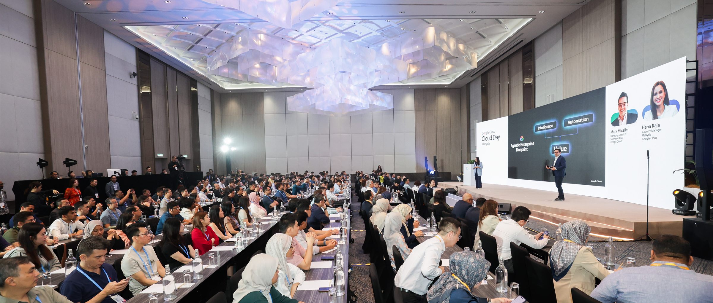 The Cloud Day Malaysia plenary in full, long conference tables under a sculptural ceiling installation facing the main stage