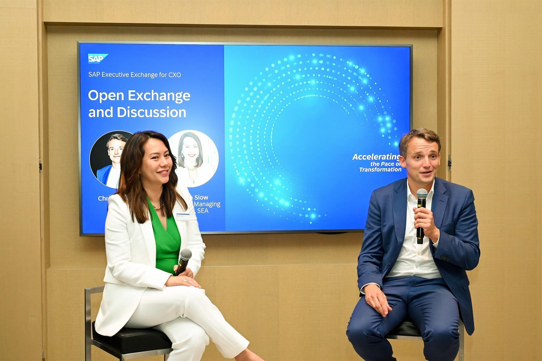 Two panellists on stools during the open exchange and discussion session, the session title on the screen behind